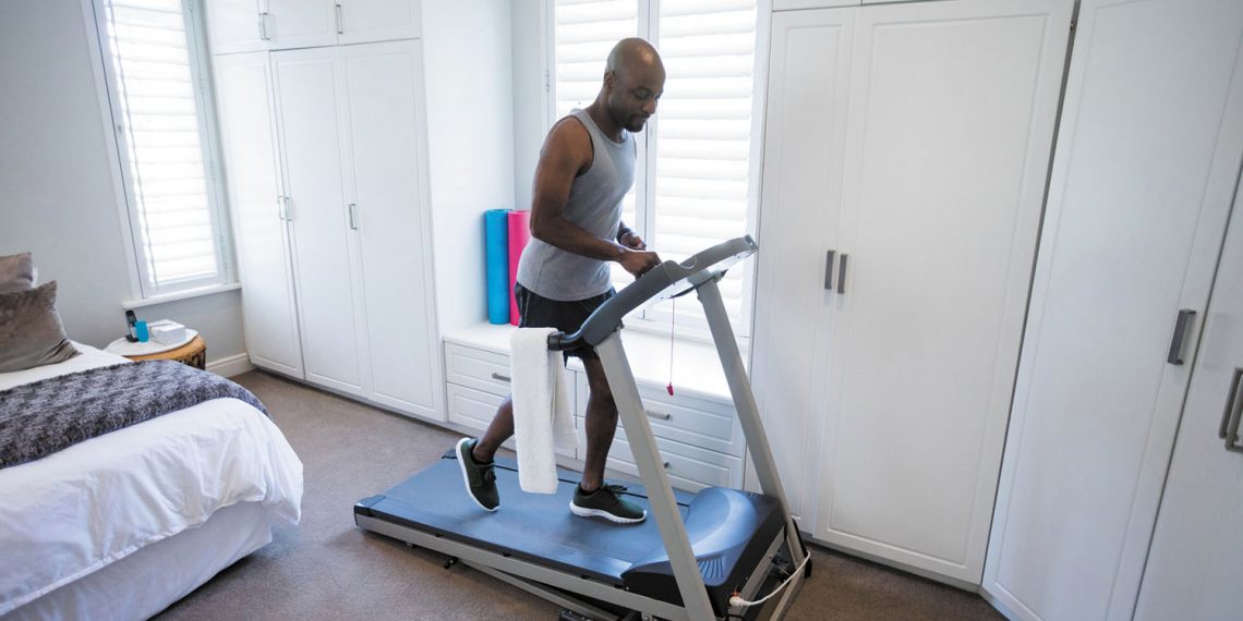 Mid section of man using smart watch while exercising on treadmill at home