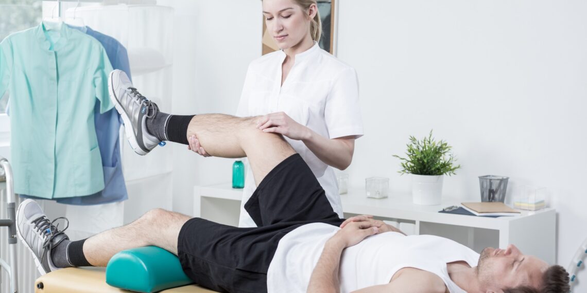 Horizontal view of female chiropractor exercising man's leg