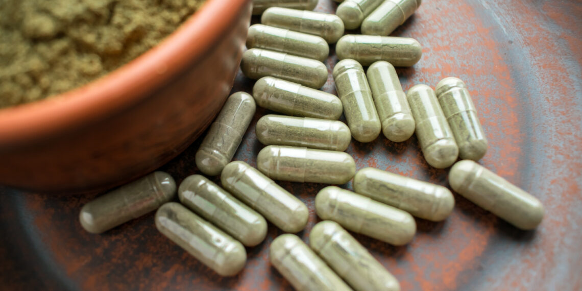 Supplement kratom green capsules and powder on brown plate. Herbal product alt-medicine kratom is  opioid. Home alternative pain remedy, opioid addiction, dangerous painkiller, overdose. Close up. Selective focus
