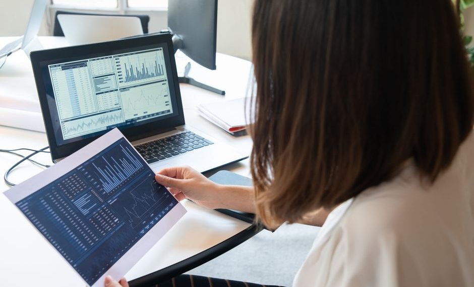 Professional in business attire analyzing financial data on computer screens in modern banking office environment.